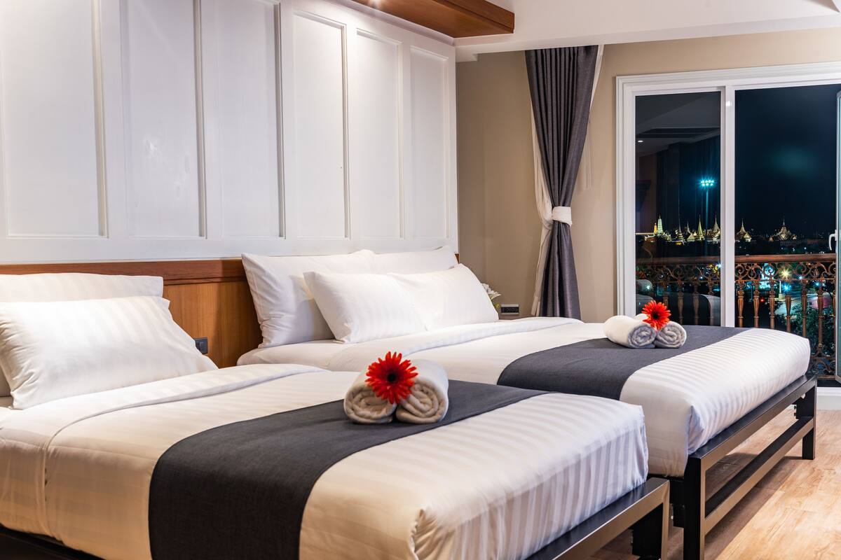 Une chambre d’hôtel avec deux lits, une grande fenêtre donnant sur le paysage urbain et un balcon avec une balustrade.