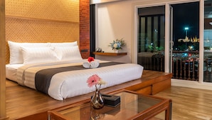 Une chambre d’hôtel avec un grand lit, une table basse en verre, un vase rempli de fleurs et une vue sur la ville la nuit.