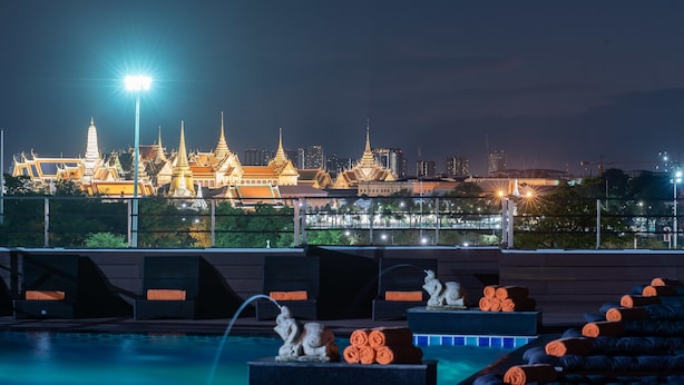 Un espace piscine aménagé sur le toit, offrant une vue sur un ensemble de temples traditionnels la nuit.