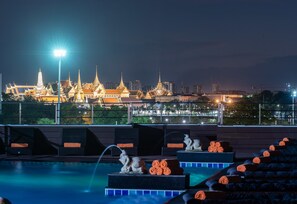 A rooftop pool area with a view of a traditional temple complex at night. - Dang Derm in The Park Khaosan (Bangkok)
