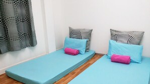 Deux lits simples avec une literie bleue et des oreillers roses, ainsi que des oreillers gris à motifs, et un plancher en bois.