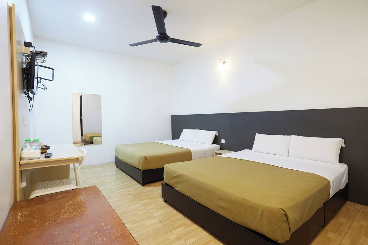 Hotelkamer met twee bedden, een bureau, een stoel, een plafondventilator en een spiegel.