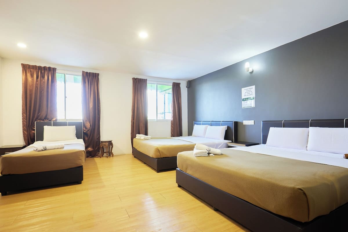 Een hotelkamer met drie bedden, houten vloeren en een donkere wand.