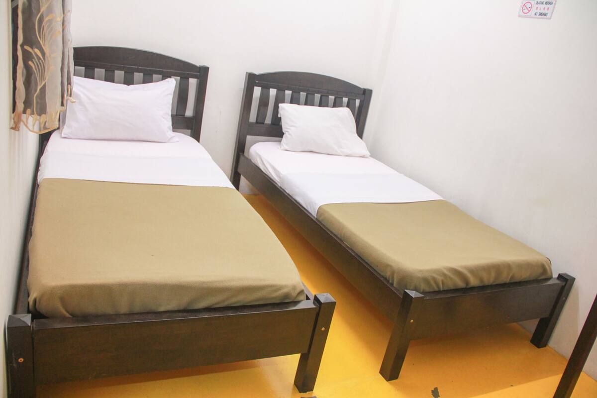 Twee eenpersoonsbedden met houten frames en witte beddengoed in een kamer met witte wanden.