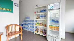 A room with a wooden bench, a refrigerator stocked with beverages, and shelves with bottled water and snacks.