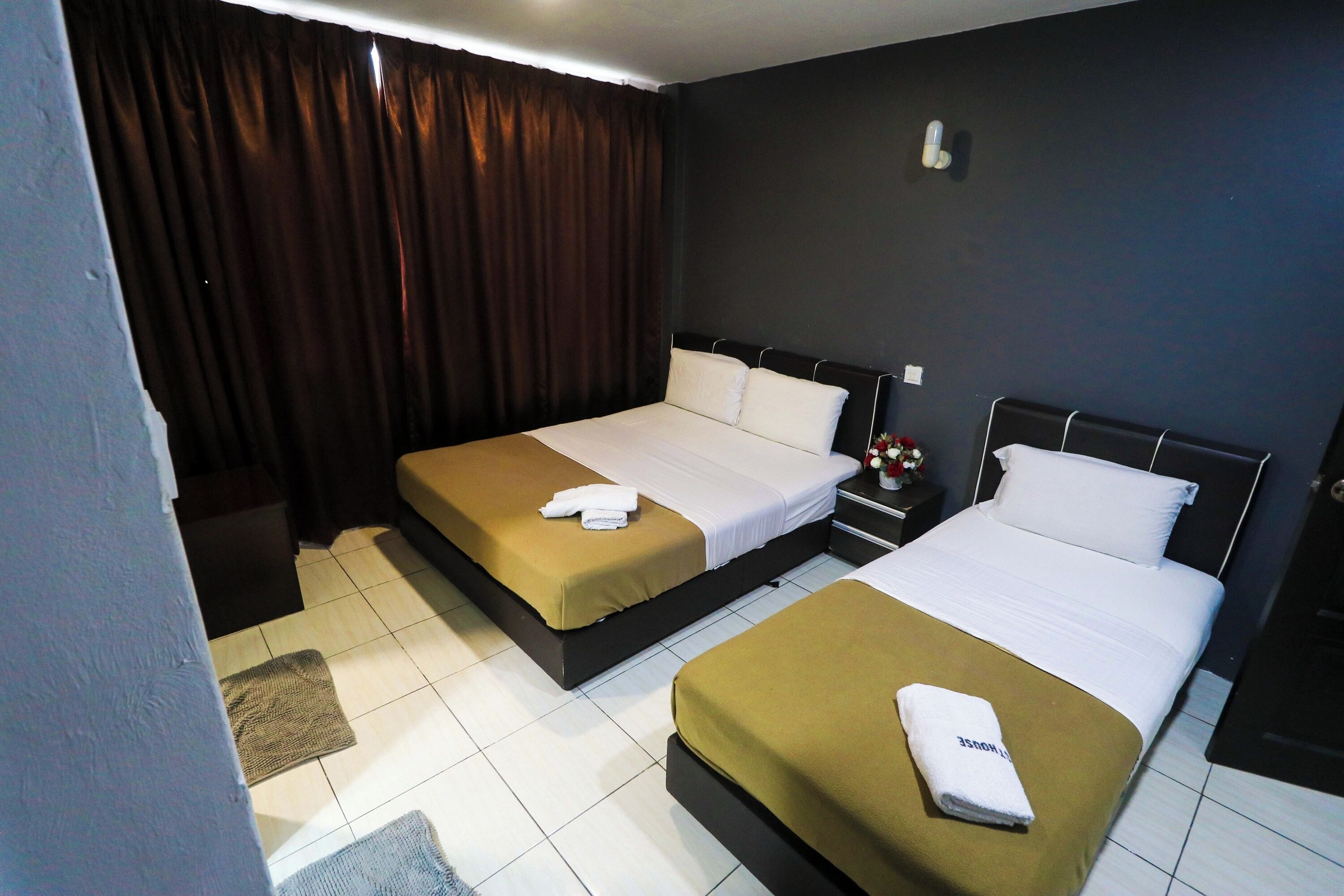 Ein Hotelzimmer mit zwei Betten, jedes mit einer braunen Bettdecke und weißen Kissen, sowie einem kleinen Nachttisch mit Blumen in einer Vase.