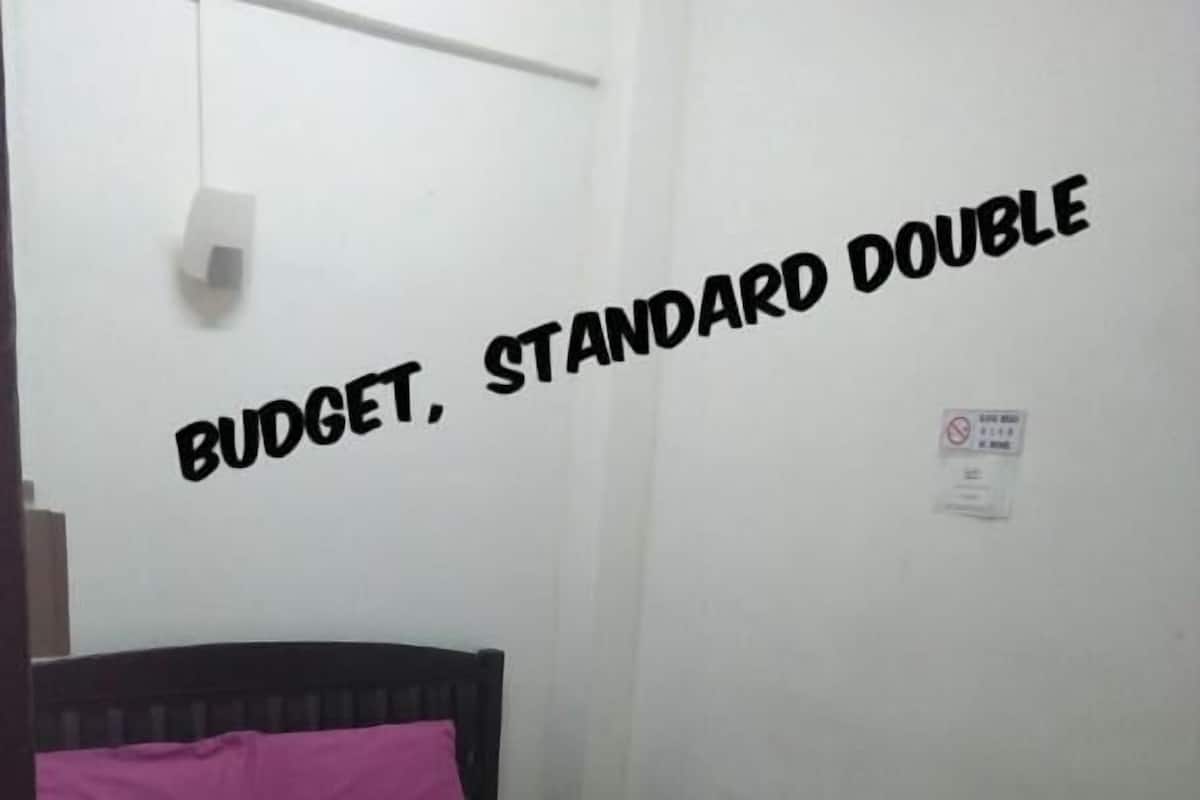 Een standaard tweepersoonskamer met een bed, een wandlamp en een rookvrij sign.