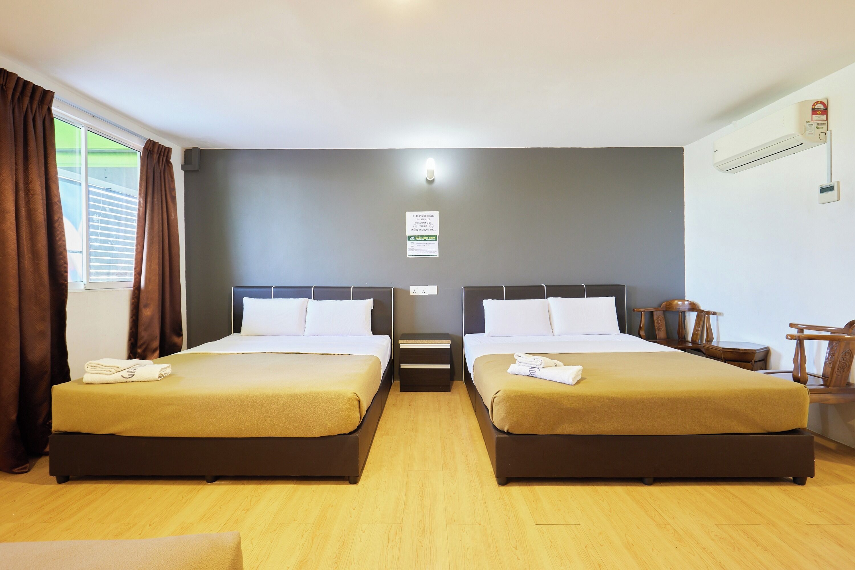 A hotel room with two beds, a nightstand, a wooden chair, and a window with curtains.