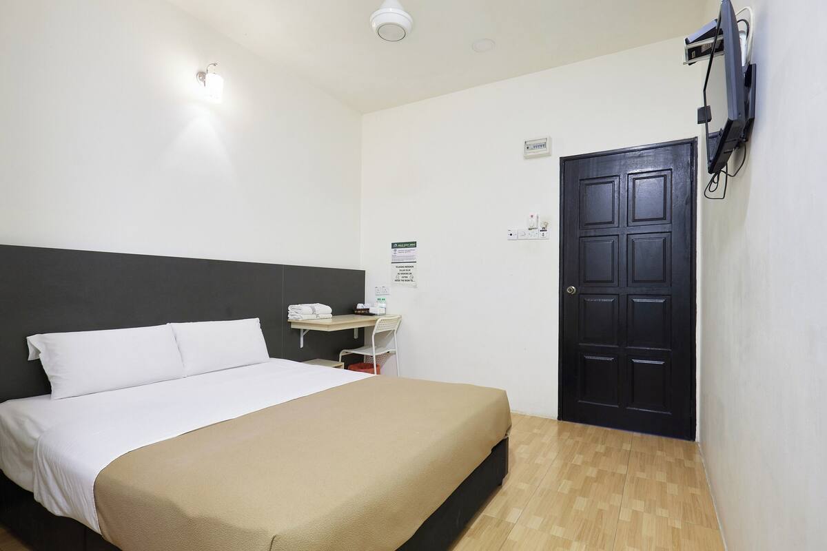 Hotelkamer met een bed, bureau, stoel, zwarte deur en een wandgemonteerde televisie.