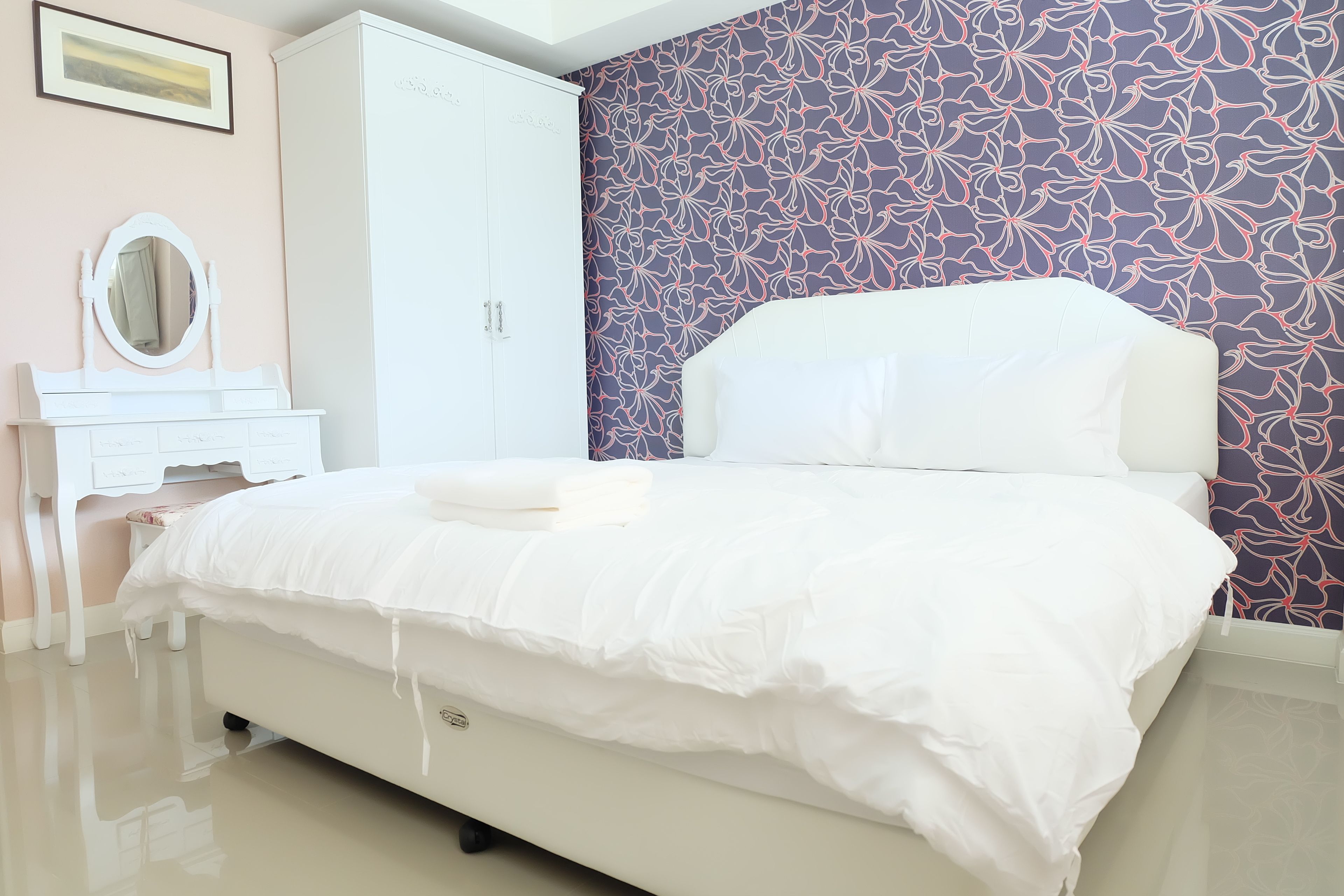 Een slaapkamer met een bed, een dressoir, een spiegel en een kledingkast.