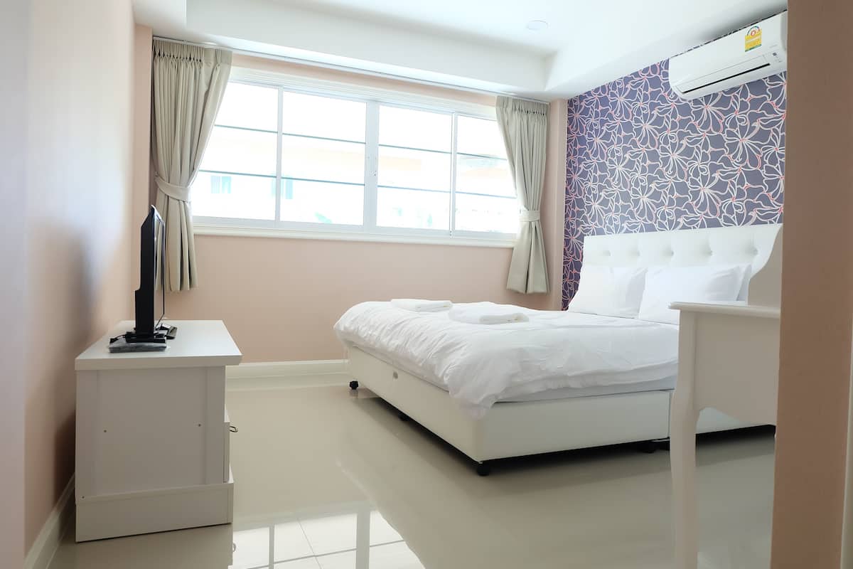 A modern bedroom with a large bed, a bedside table, a TV, and a window with curtains.