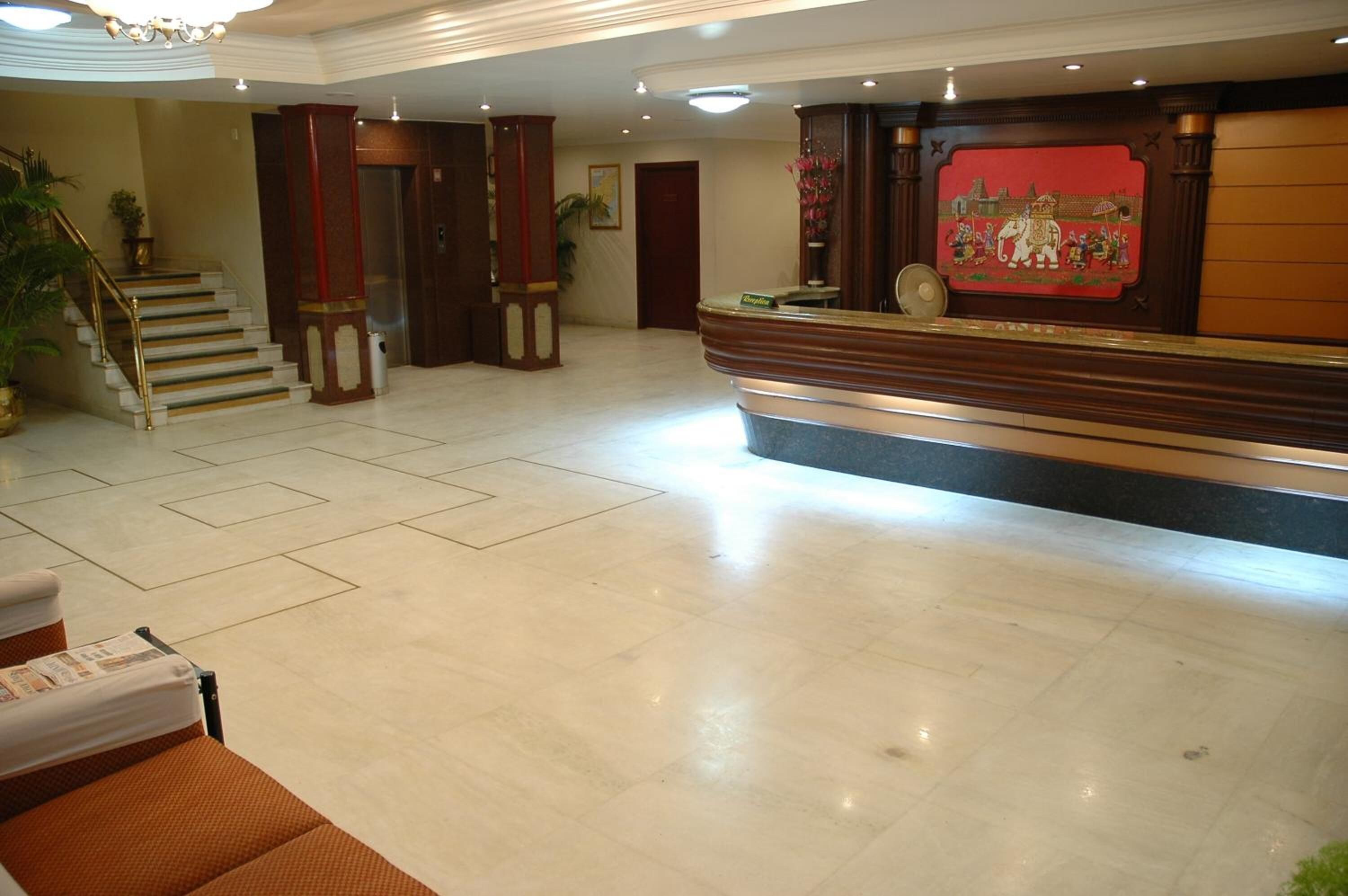 A spacious lobby with a reception desk, a staircase, and a large potted plant.