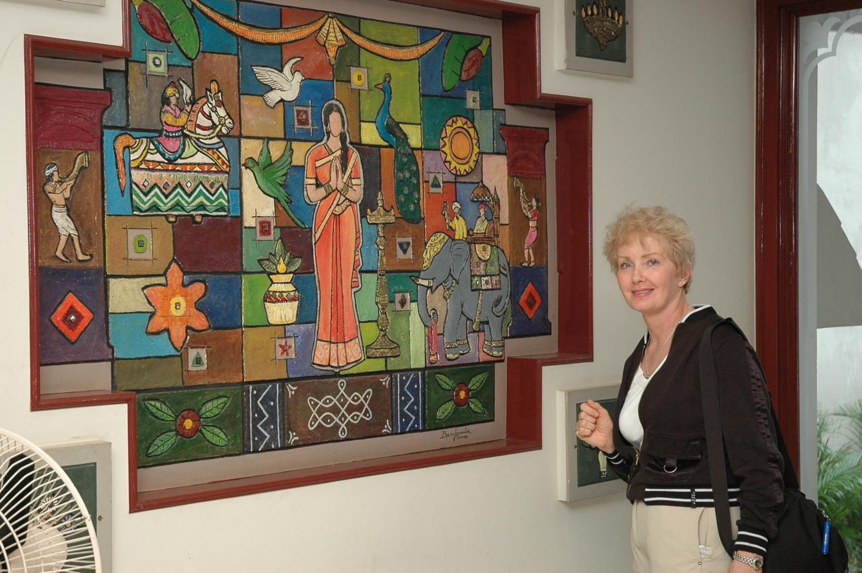 Une femme se tient devant une œuvre d'art en mosaïque aux couleurs vives.