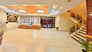 Un'ampia hall con reception, un divano decorato, una scala e un'ampia finestra.