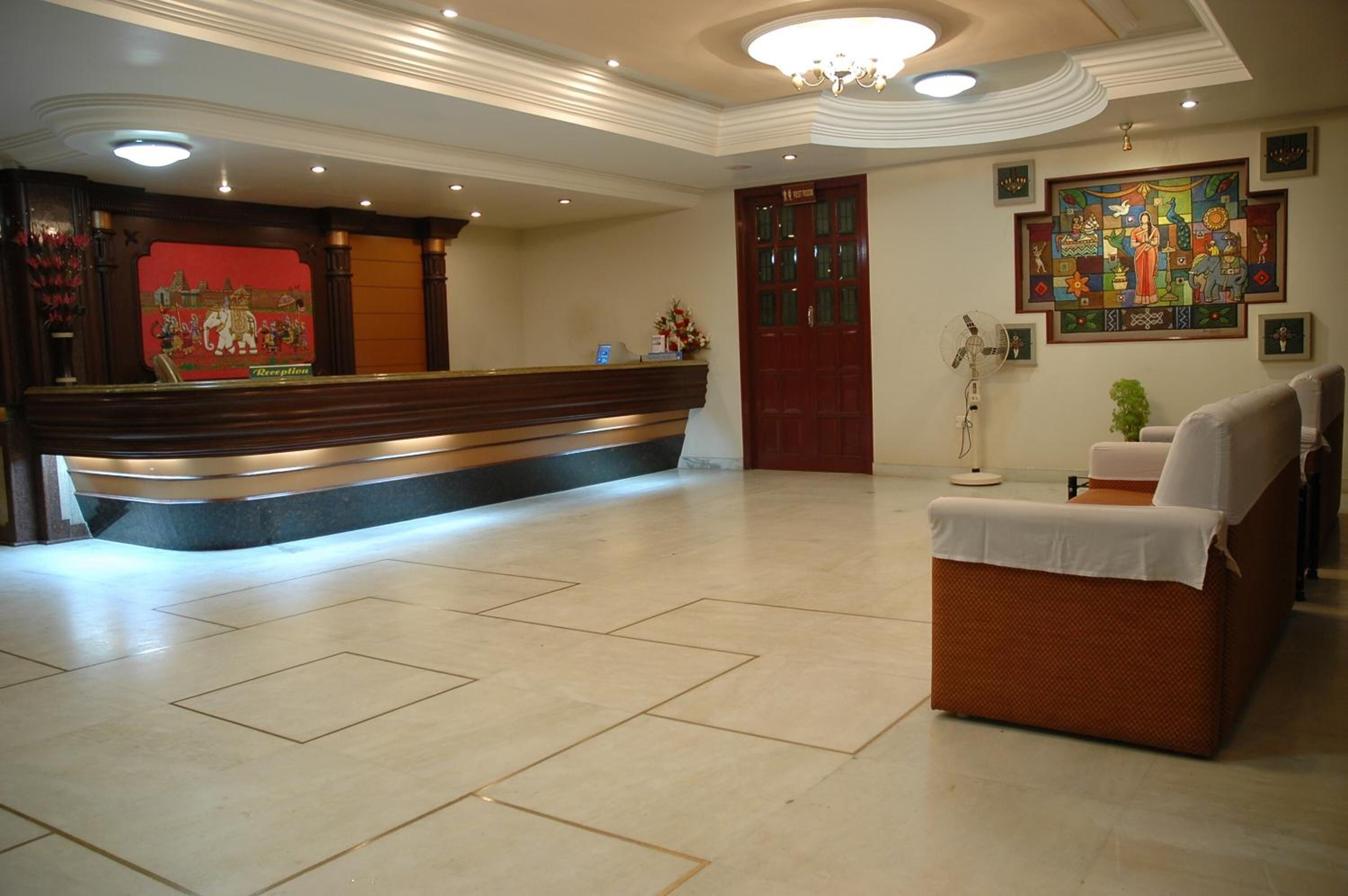 Zona de recepción con mostrador, cartel de recepción, una pintura grande, una puerta y un área de descanso con mesa y sillas.