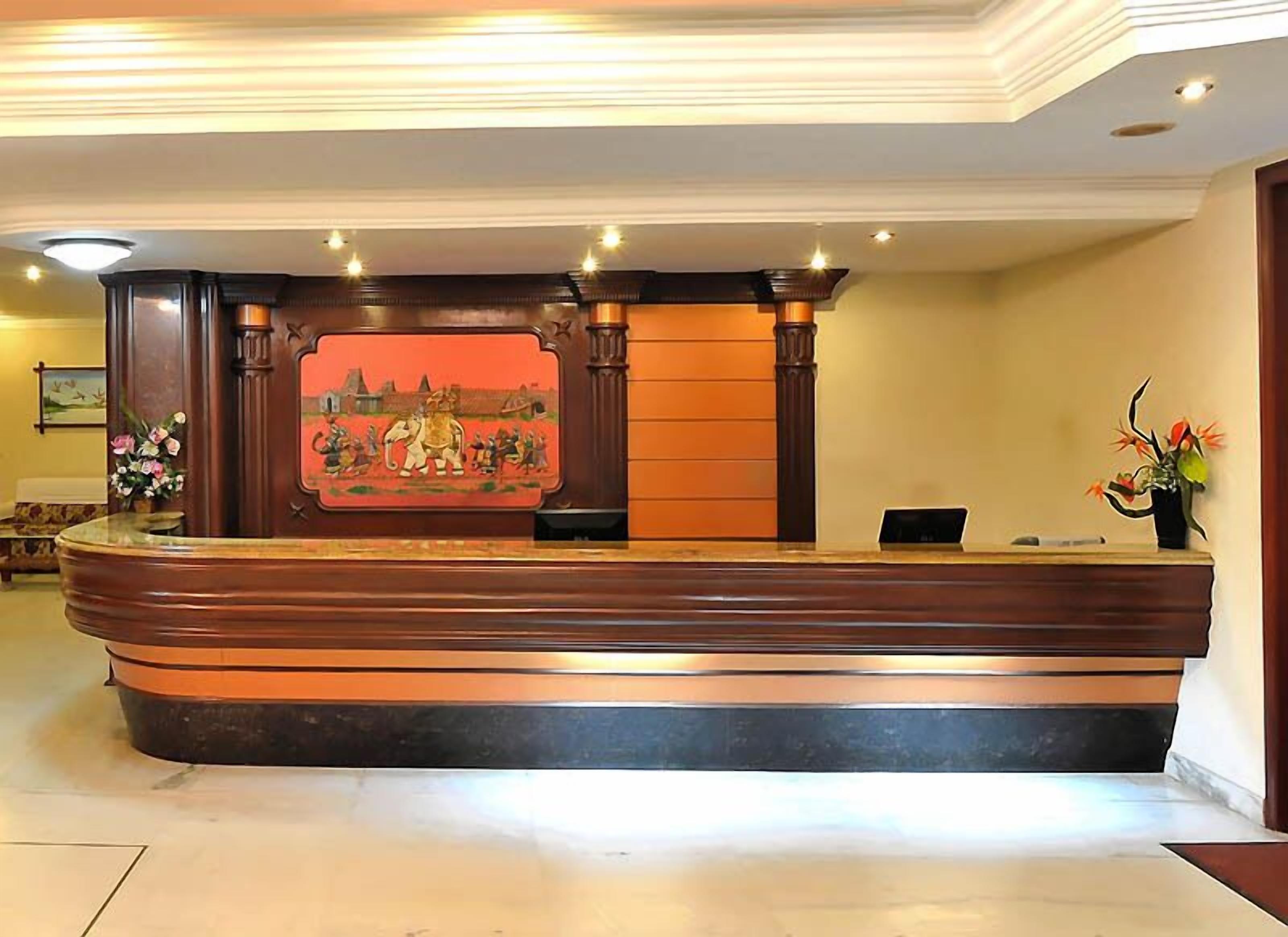 Un mostrador de recepción con un fondo decorativo, un florero con flores y un cuadro en la pared.