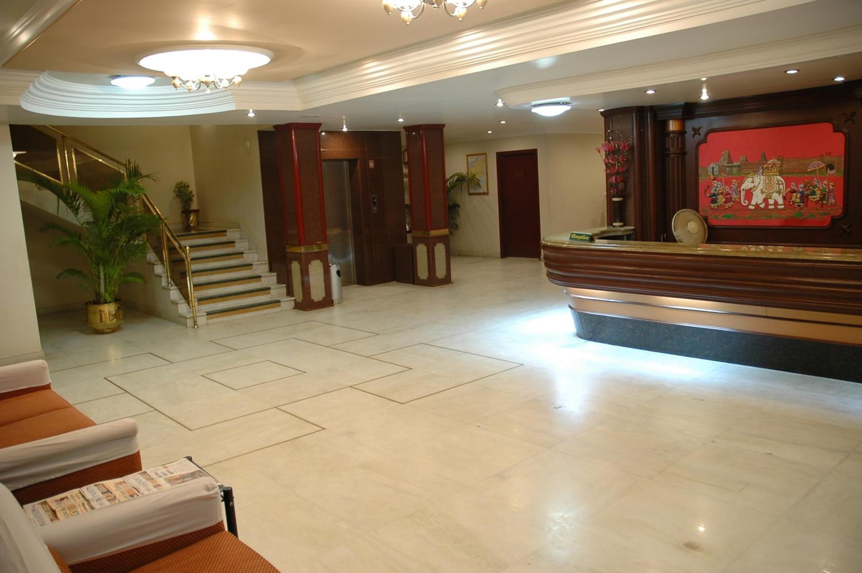 A hotel lobby with a reception desk, a staircase with a golden handrail, and a potted plant.