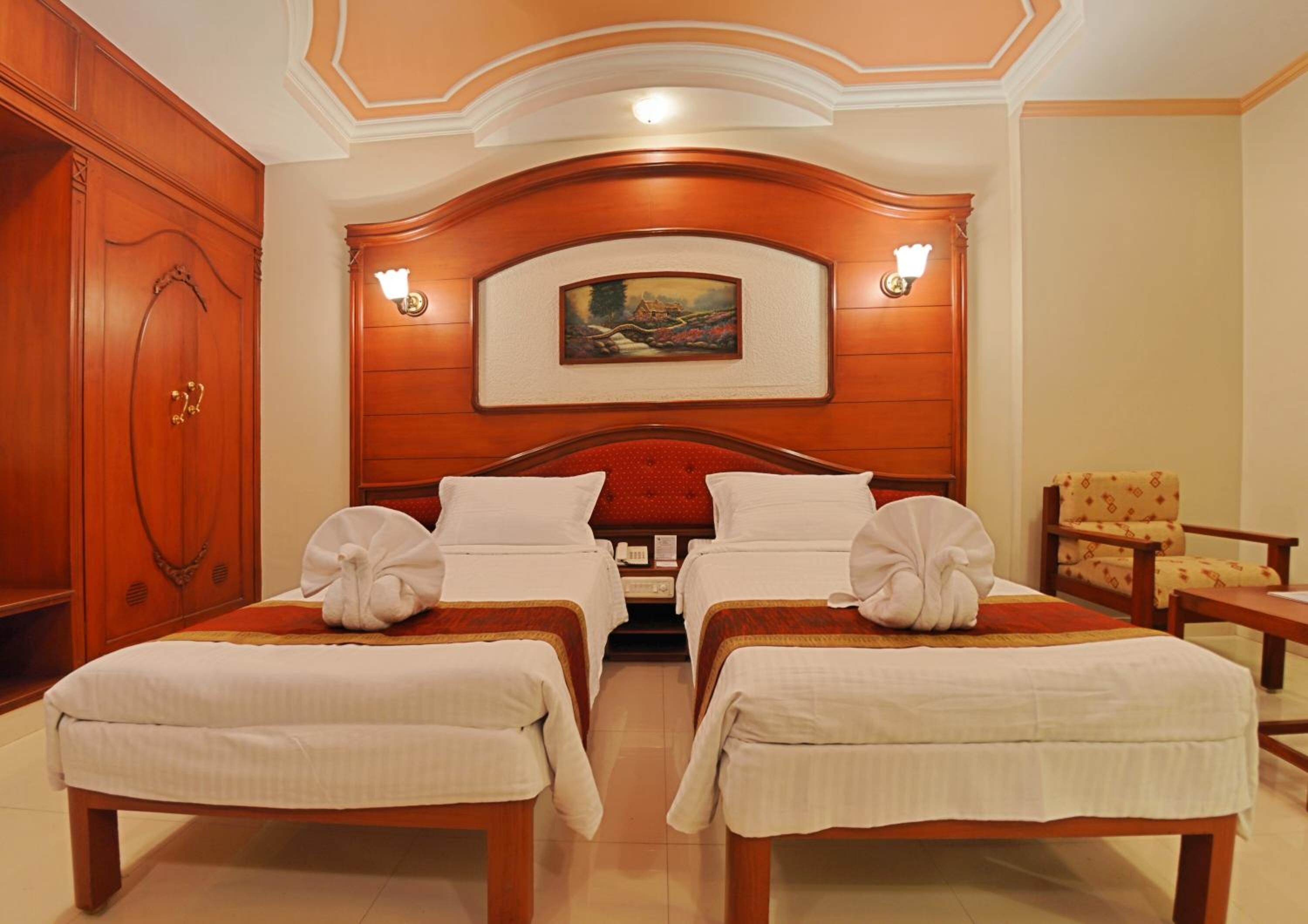 A hotel room with two beds, a wooden headboard, a painting above the beds, and a chair in the corner.