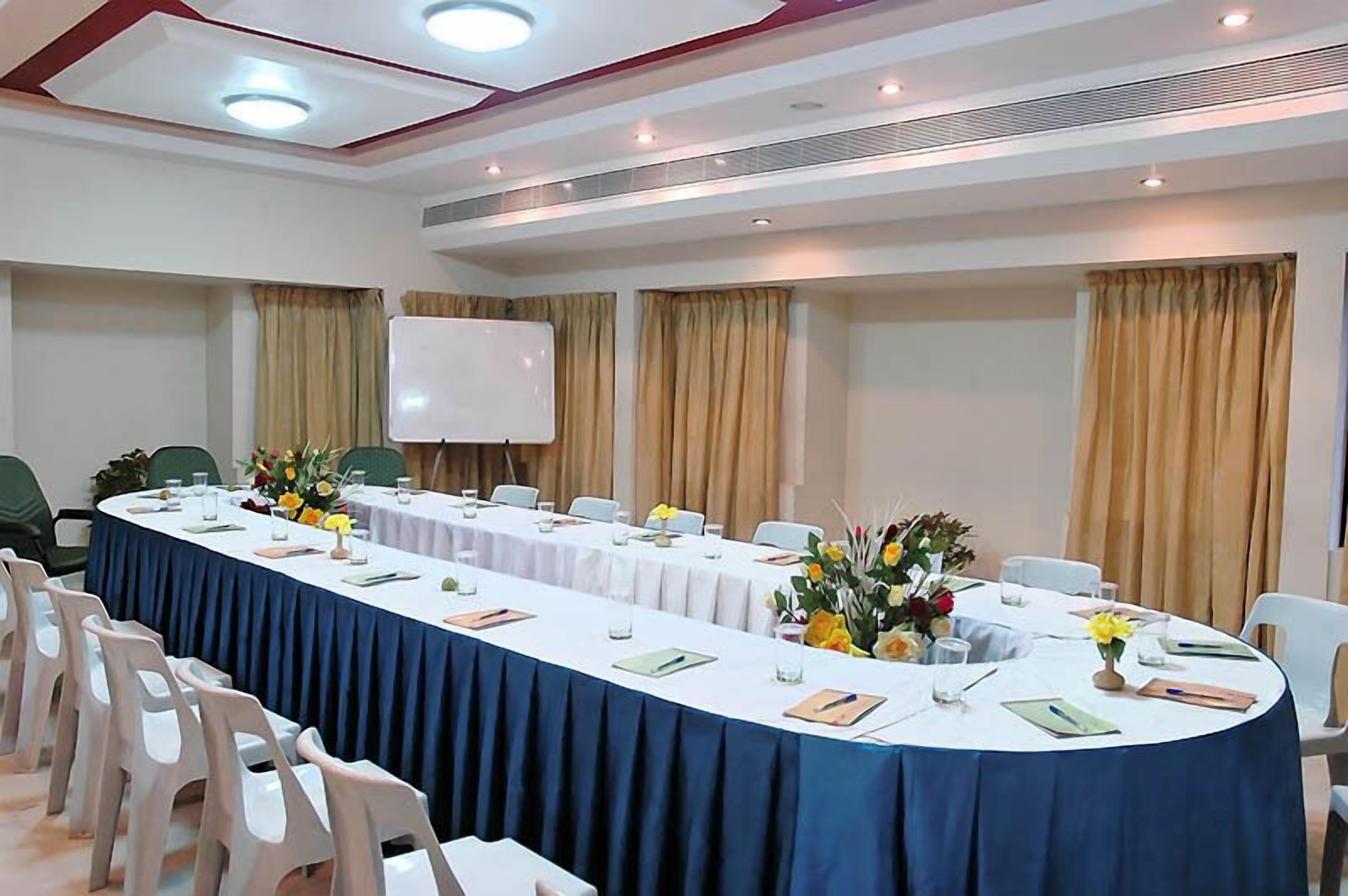 A conference room with a long table, chairs, a whiteboard, and curtains.