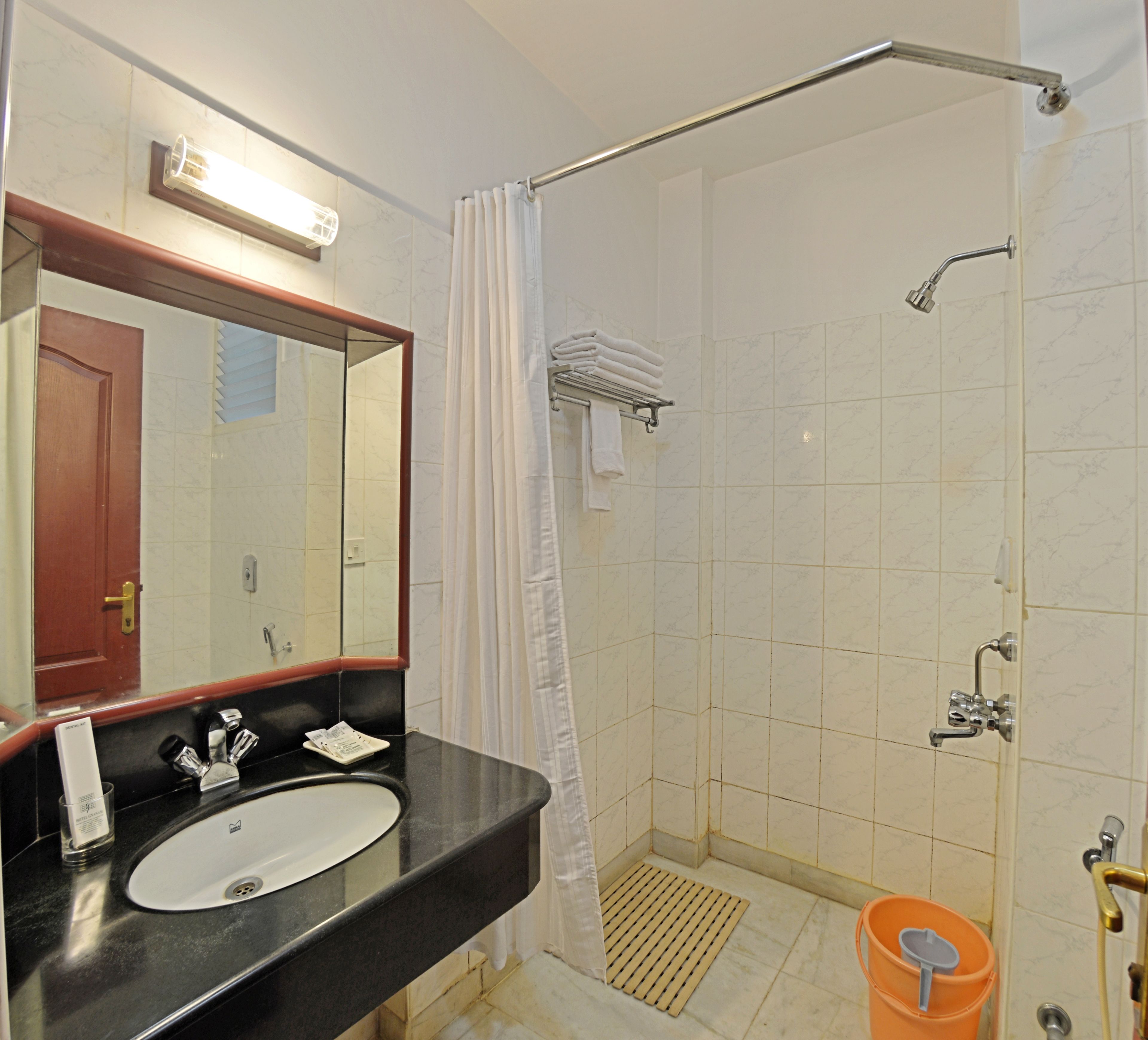 Une salle de bain avec un lavabo, un miroir, une douche et un petit seau orange.