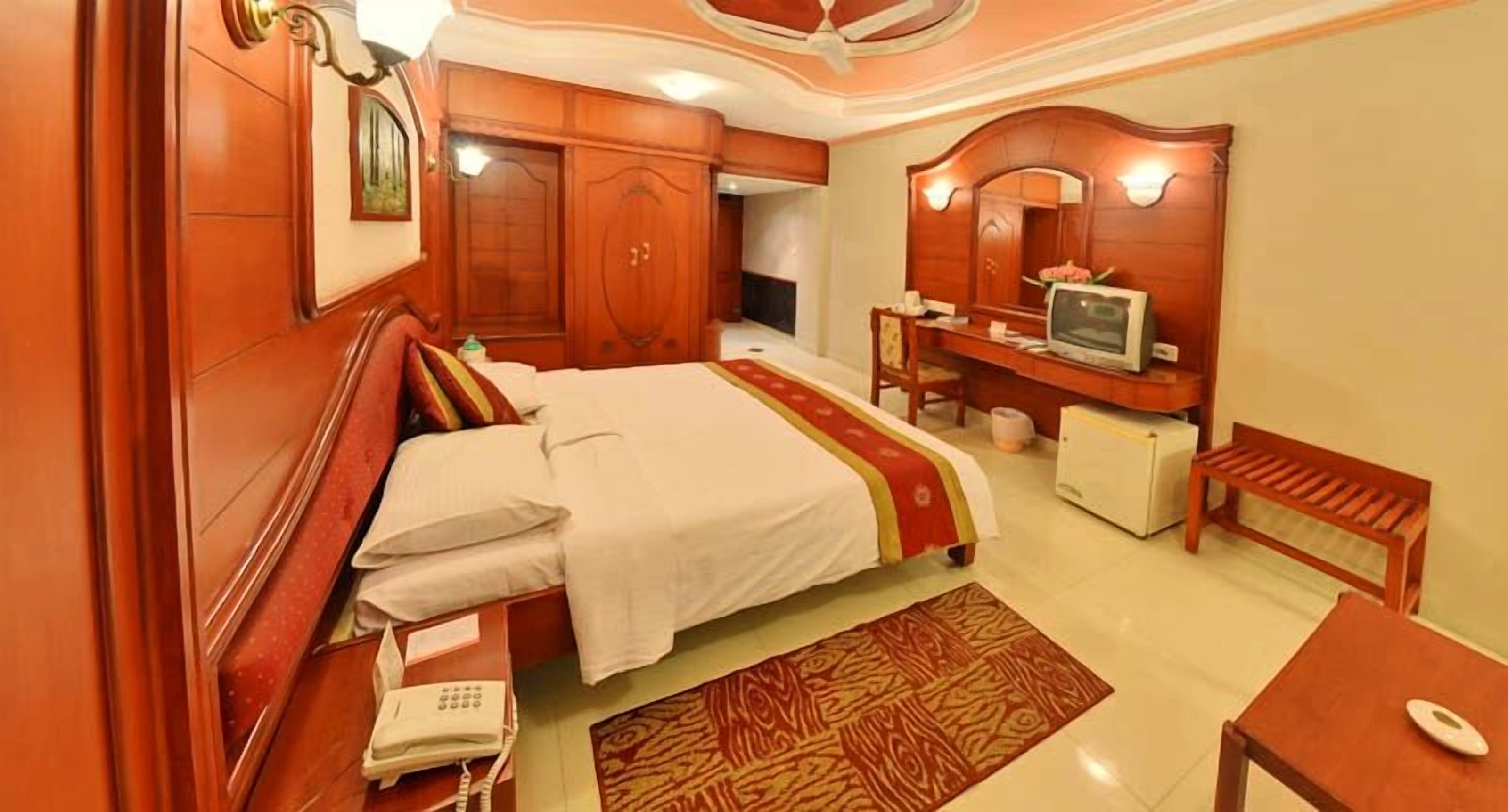Een hotelkamer met een bed, een bureau met een computer, een stoel, een telefoon en een klein tafeltje.