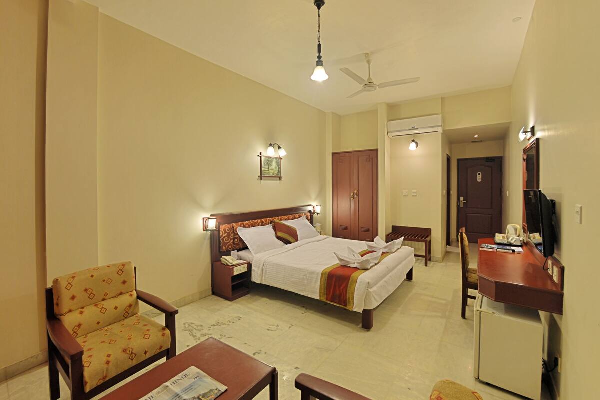 A hotel room with a bed, two chairs, a desk, a television, and a wardrobe.