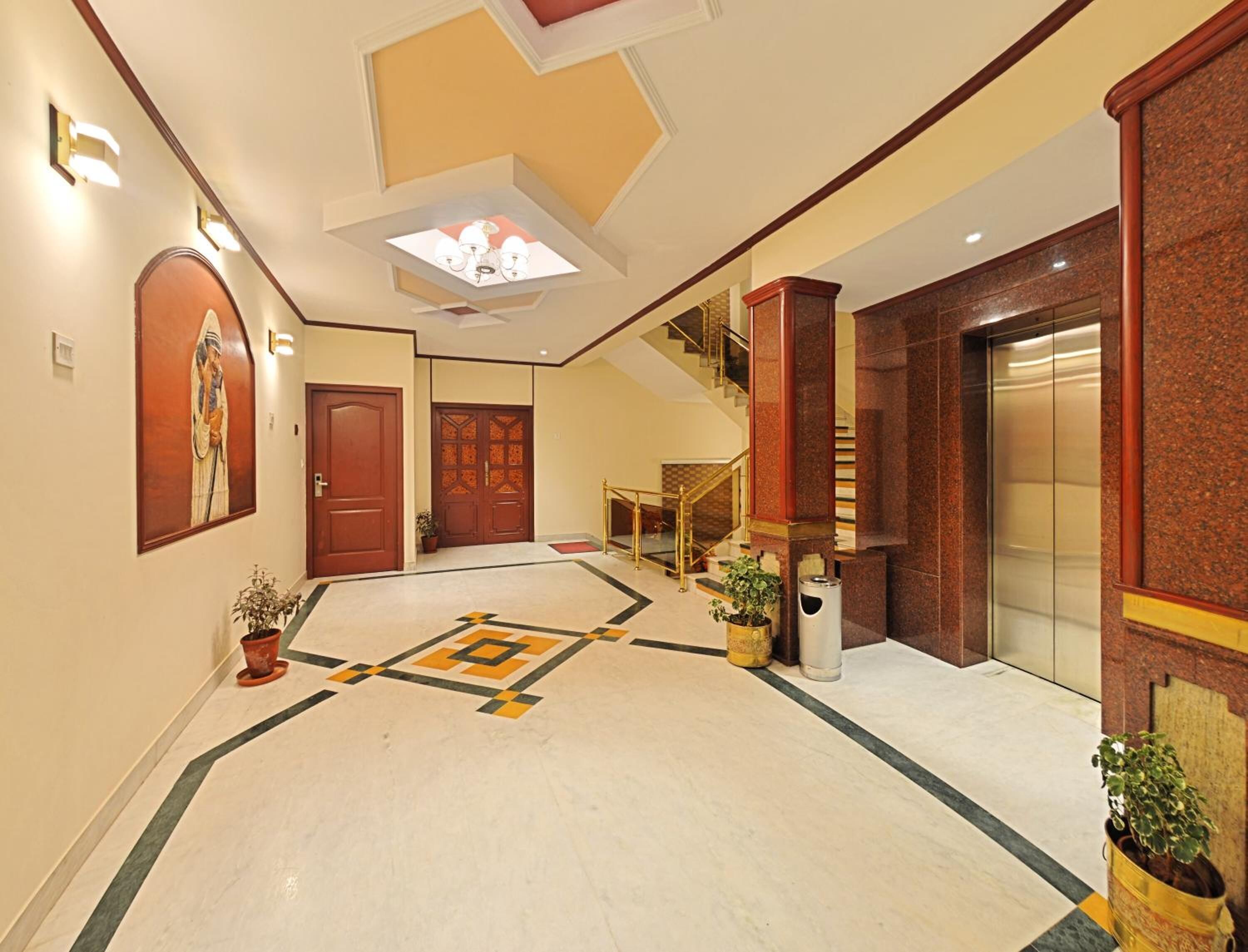 A hotel lobby with a marble floor, a staircase, a reception desk, and a large wall-mounted artwork.
