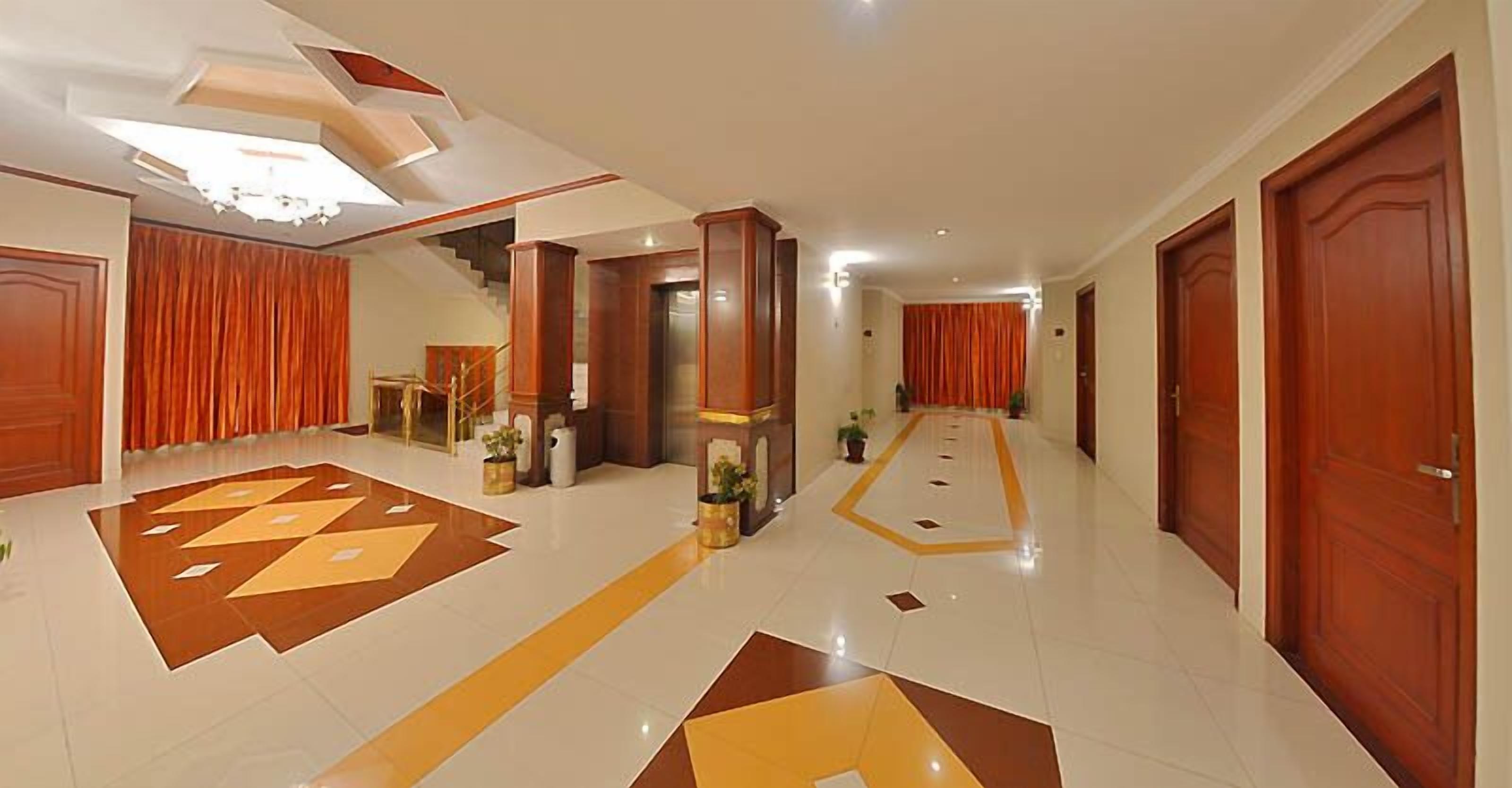 Um hall de hotel com piso de padrão geométrico, portas de madeira e uma escada.