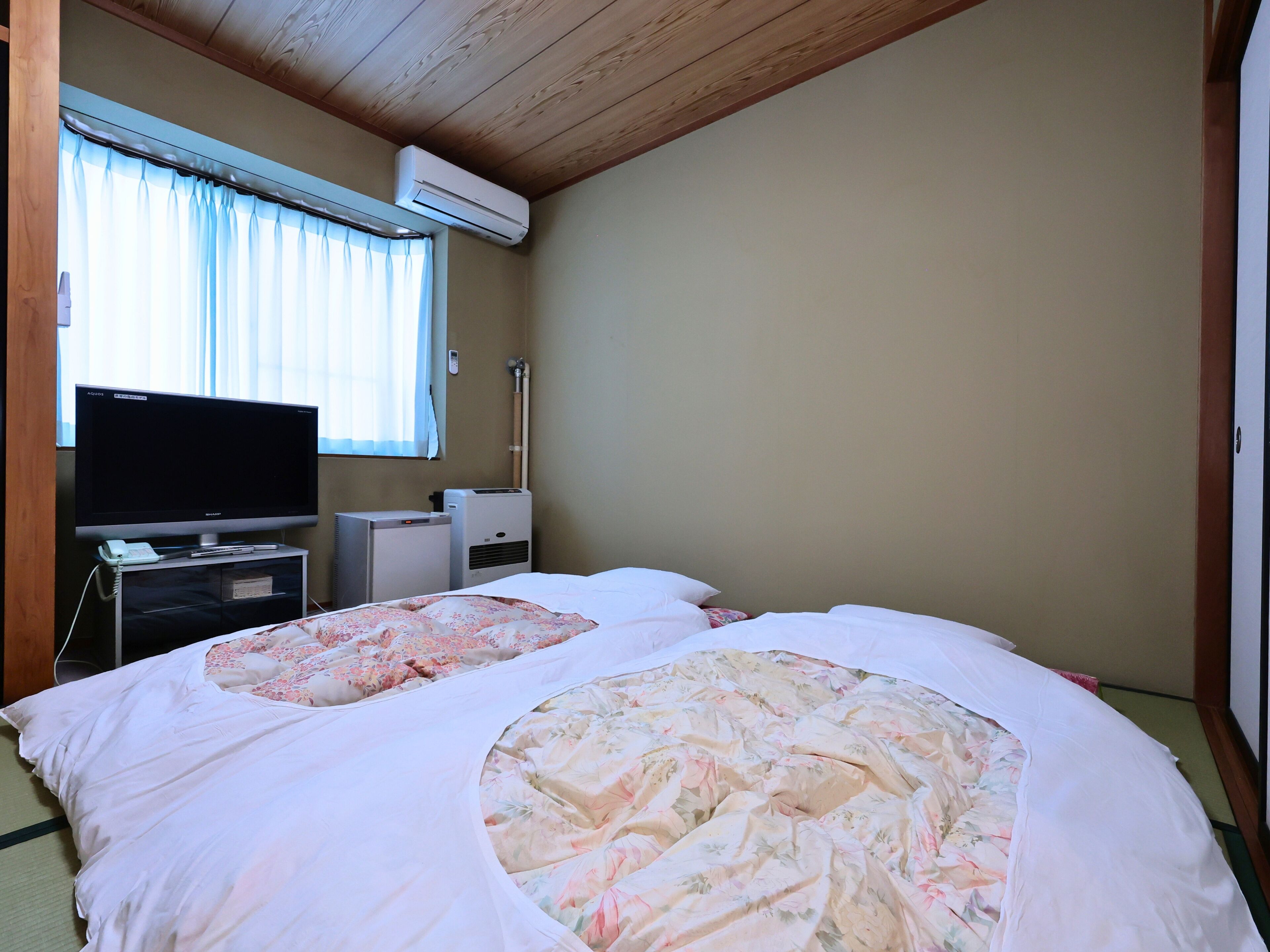A hotel room with two beds, a television, an air conditioner, and a window with curtains.