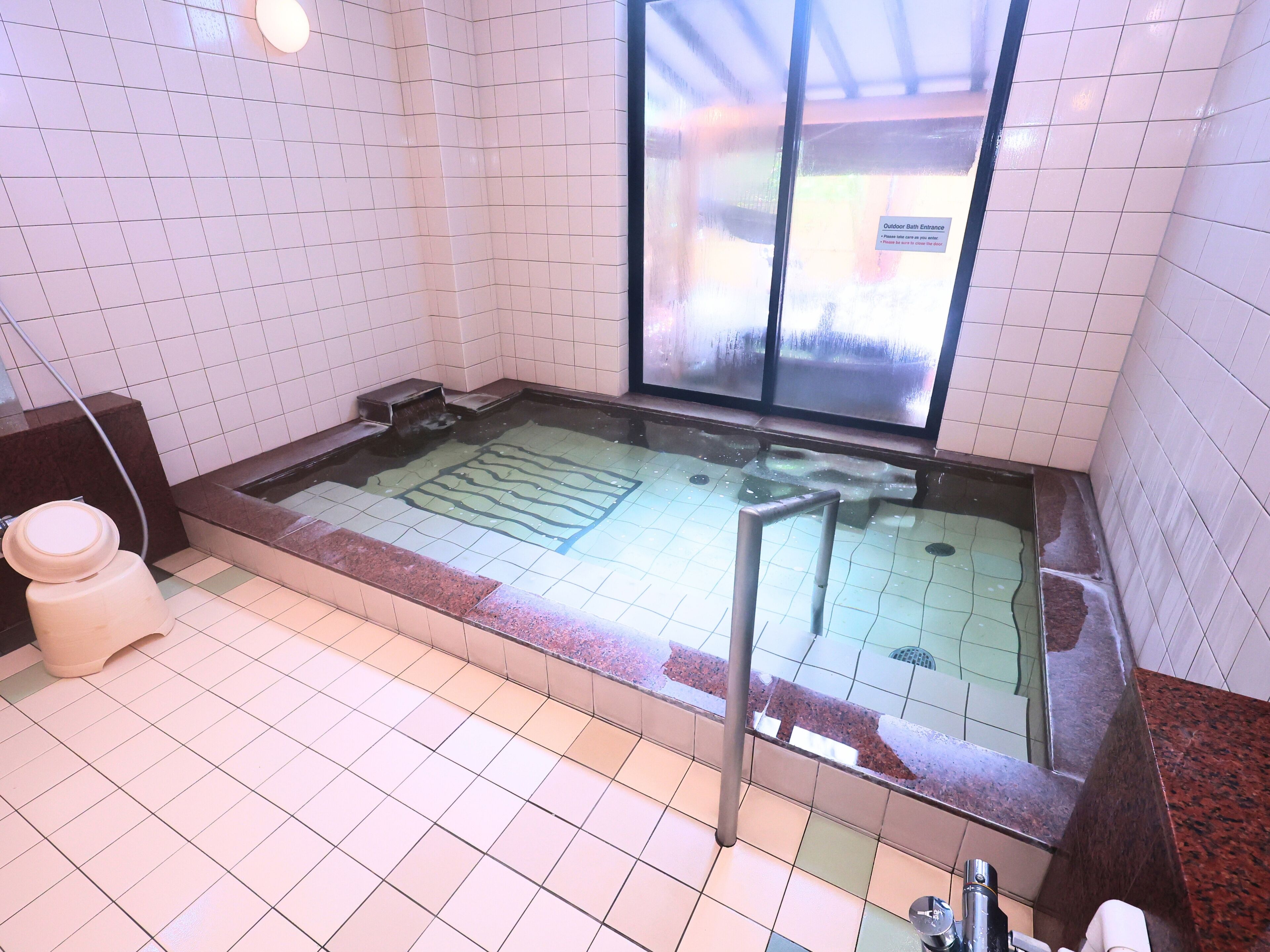 A spa area with a large hot tub, tiled walls, and a glass door leading outside.