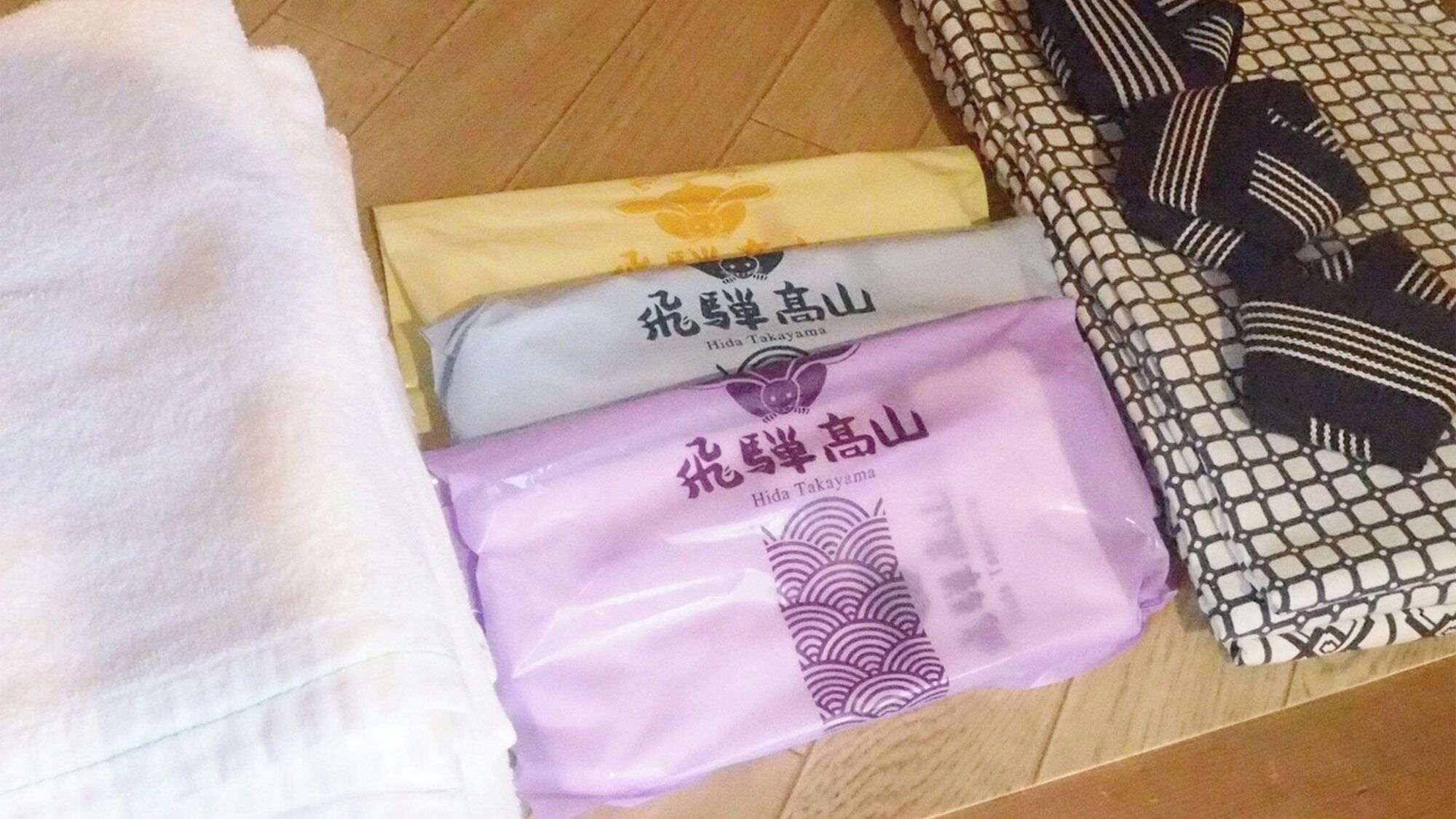 A bed with a white blanket, a yellow pillow, and a purple pillow with Japanese characters.