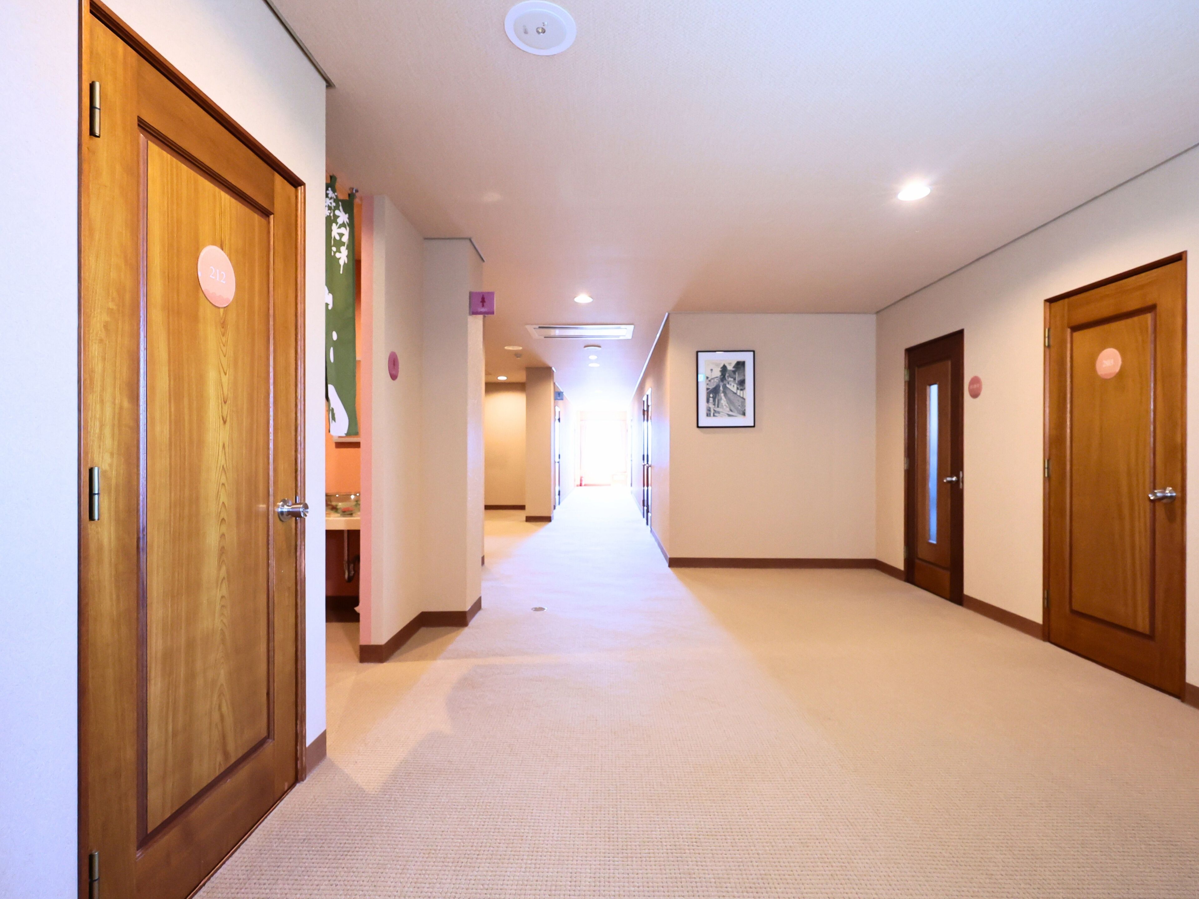 Un pasillo de hotel con puertas de madera, suelo alfombrado y un cuadro enmarcado en la pared.