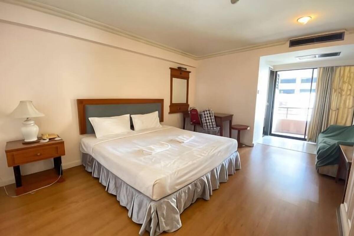 Un cuarto de hotel con una cama grande, una mesita de noche con lámpara, una silla, un escritorio y vistas al exterior.