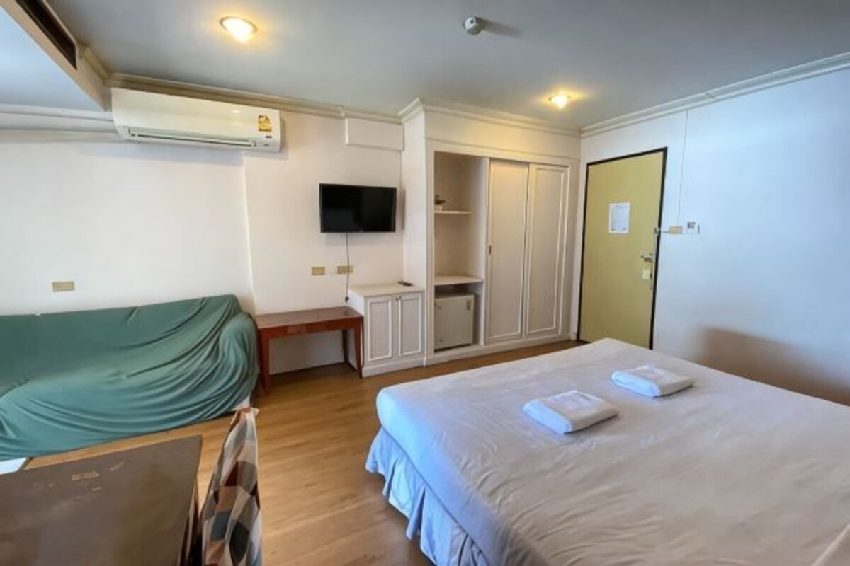 A hotel room with a bed, a desk, a television, a wardrobe, and an air conditioning unit.