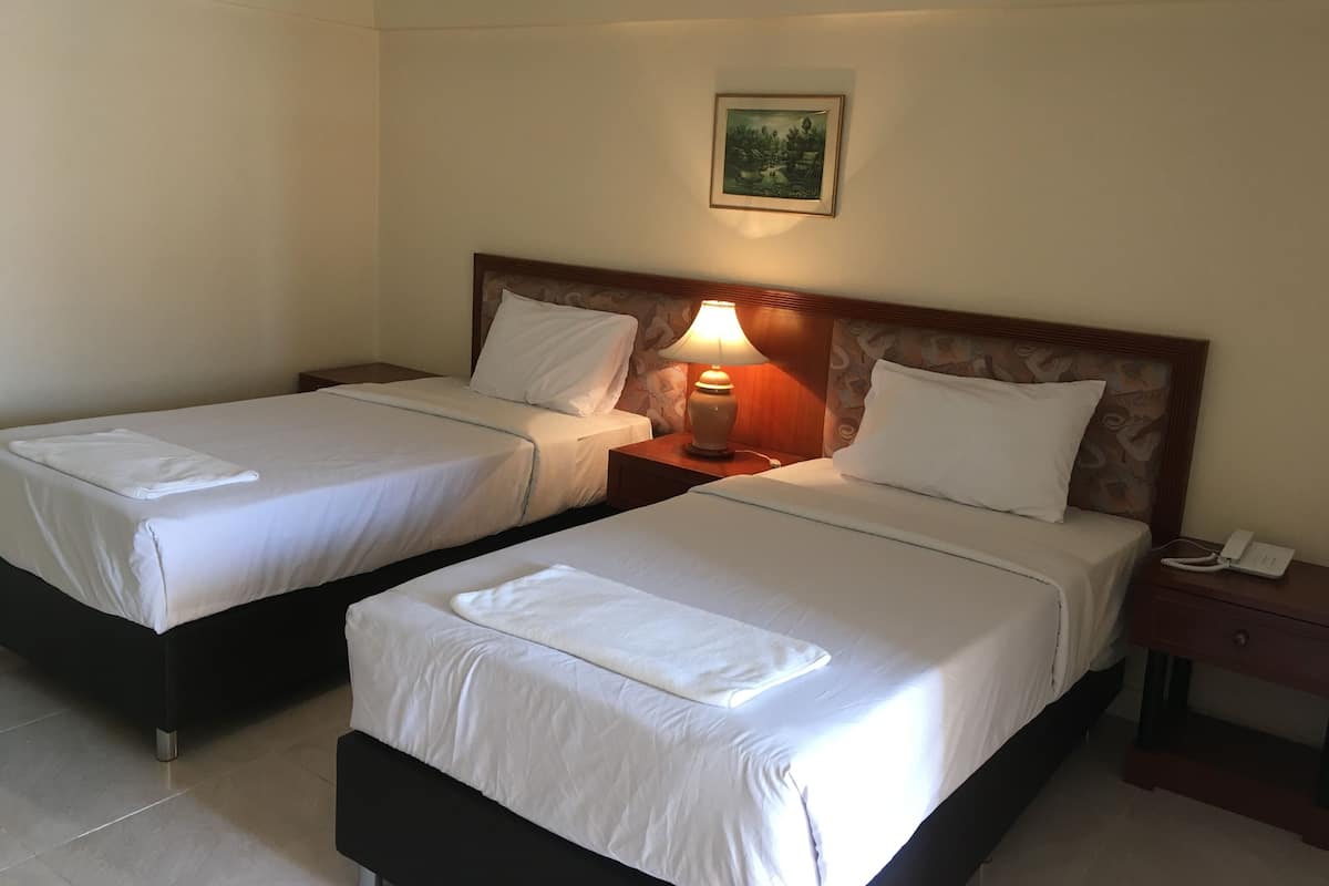 Habitación de hotel con dos camas, una mesita de noche con una lámpara, un cuadro en la pared y un teléfono sobre la mesita.