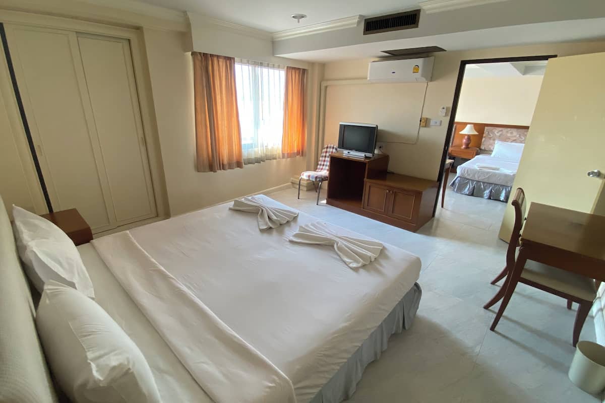 Habitación de hotel con una cama grande, un escritorio con televisor, un armario y un baño visible a través de una puerta abierta.