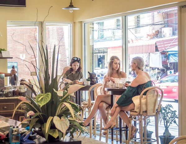 A cafe with large windows, wicker furniture, and indoor plants.