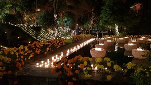 Un jardin nocturne, avec des allées bordées de fleurs et d’une multitude de bougies, créant une atmosphère paisible.