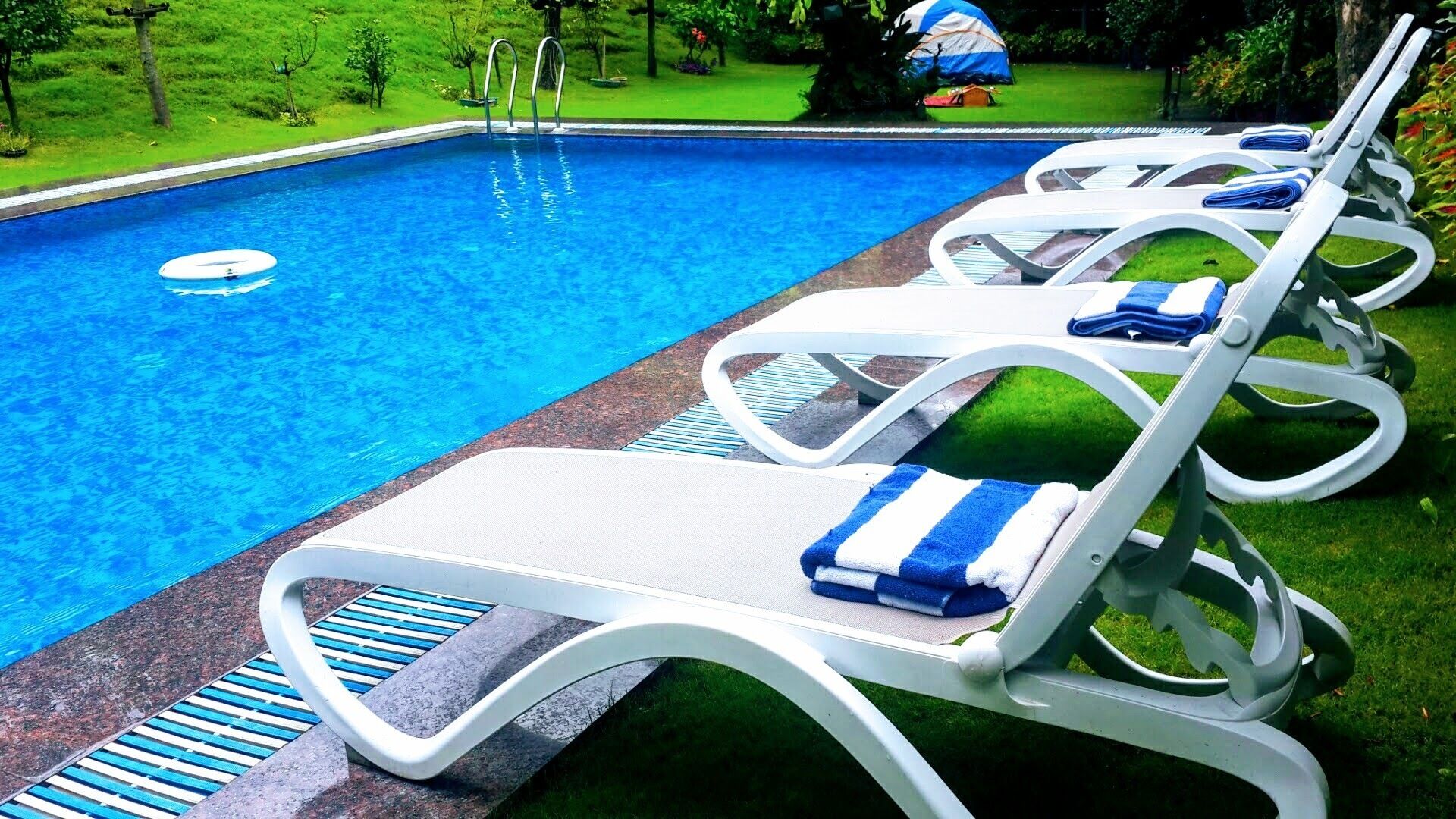 A swimming pool with white lounge chairs and blue towels.