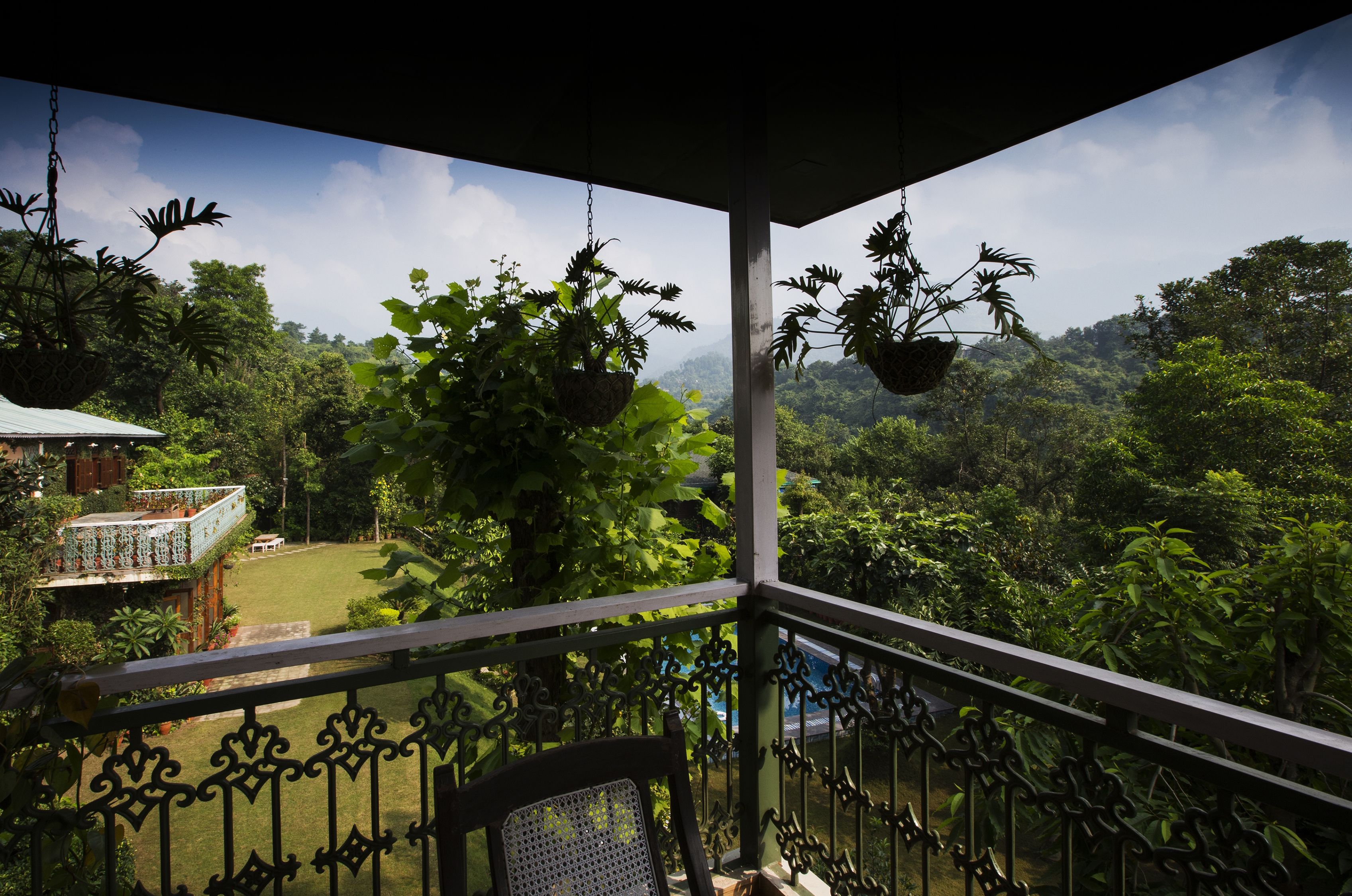 Un balcón con macetas colgantes, vistas a un paisaje verde exuberante y un edificio con techo verde al fondo.