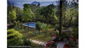 Une piscine entourée d’une végétation luxuriante et d’arbres, avec une chaîne de montagnes en arrière-plan.
