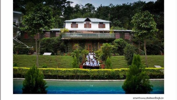 Un bâtiment à deux étages doté d’un balcon, entouré d’une végétation luxuriante et d’une piscine.