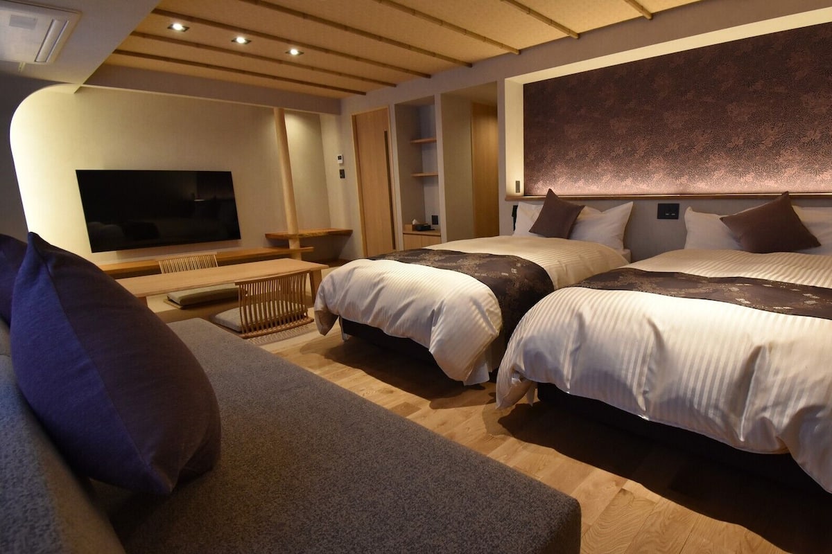 A hotel room with two beds, a sofa, a TV, and a wooden ceiling.