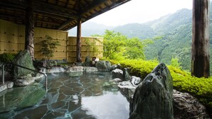 Un onsen japonés tradicional con una bañera de piedra rodeada de rocas y estructuras de bambú.