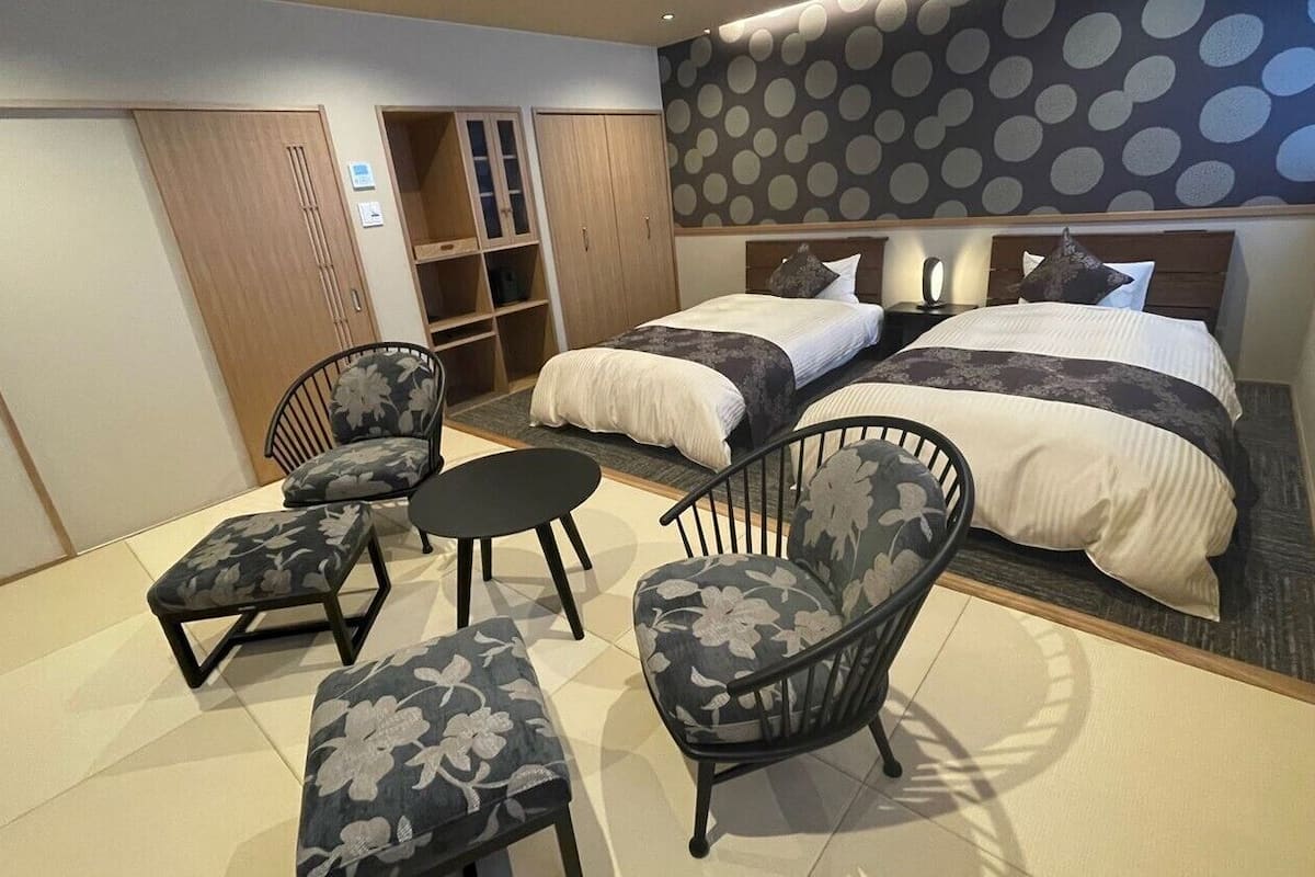 A hotel room with two beds, a seating area with chairs, a wardrobe, and a polka dot wall.