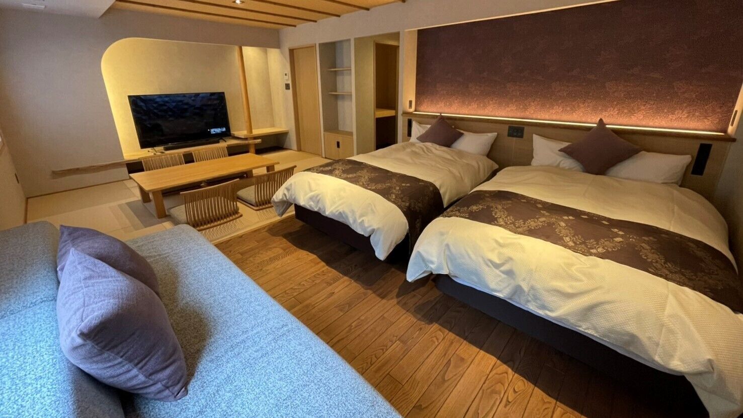 A hotel room with two beds, a TV, a desk, and a sofa.