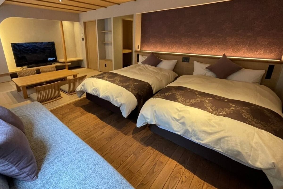 A hotel room with two beds, a TV, a desk, and a sofa.