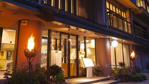 Un hotel con balcón, entrada iluminada y jardín con plantas.