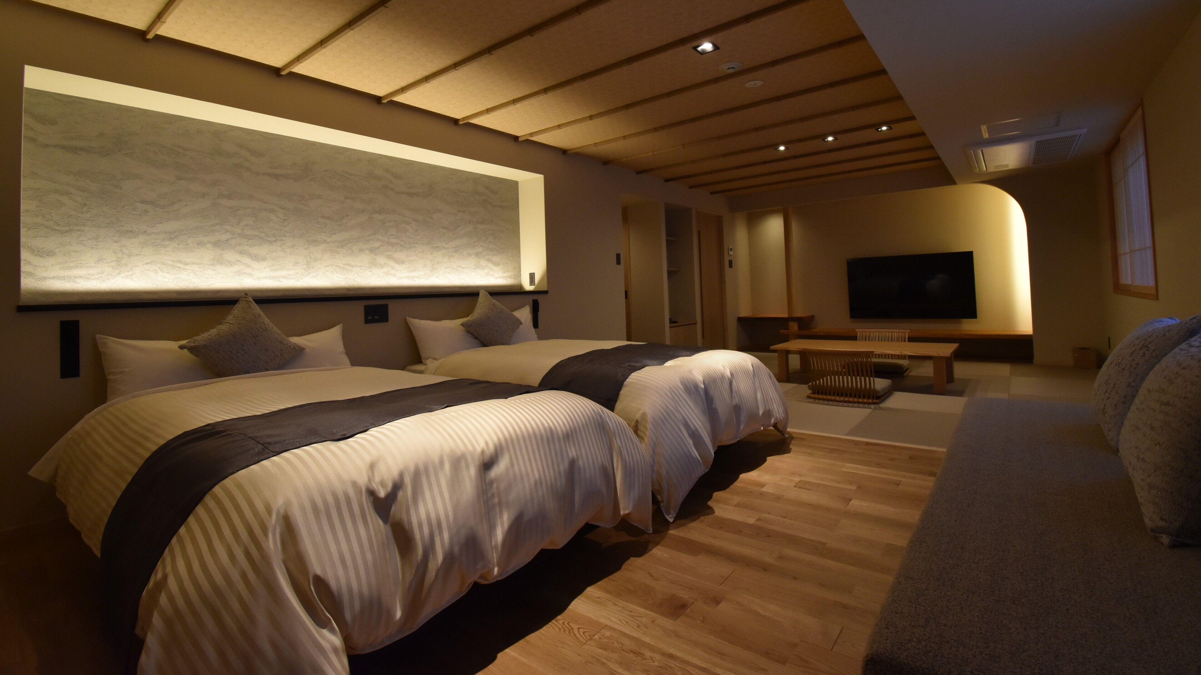 A modern hotel room with a large bed, a TV, and a seating area.