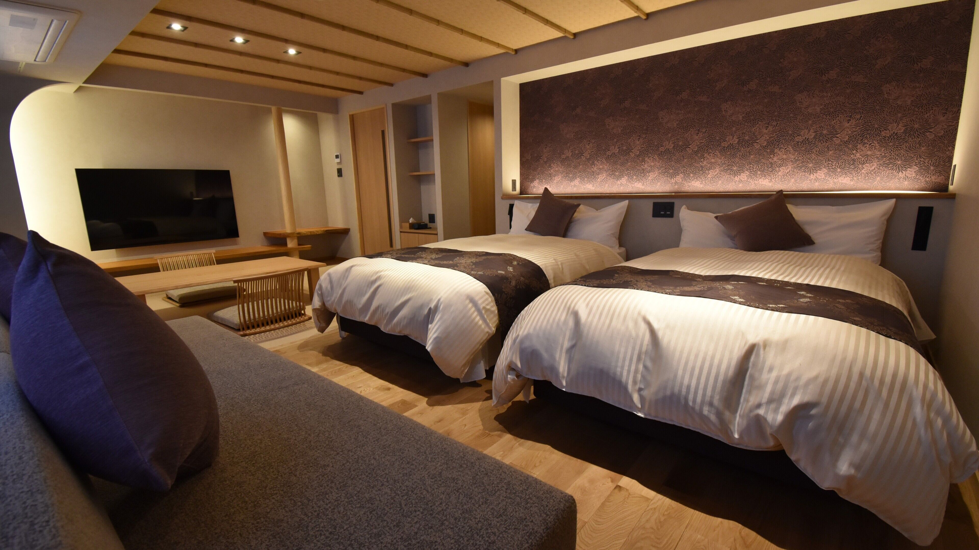 A hotel room with two beds, a TV, a sofa, and a desk.
